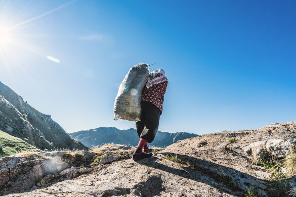 Woman carrying a bag of fresh cut grass up a steep hill